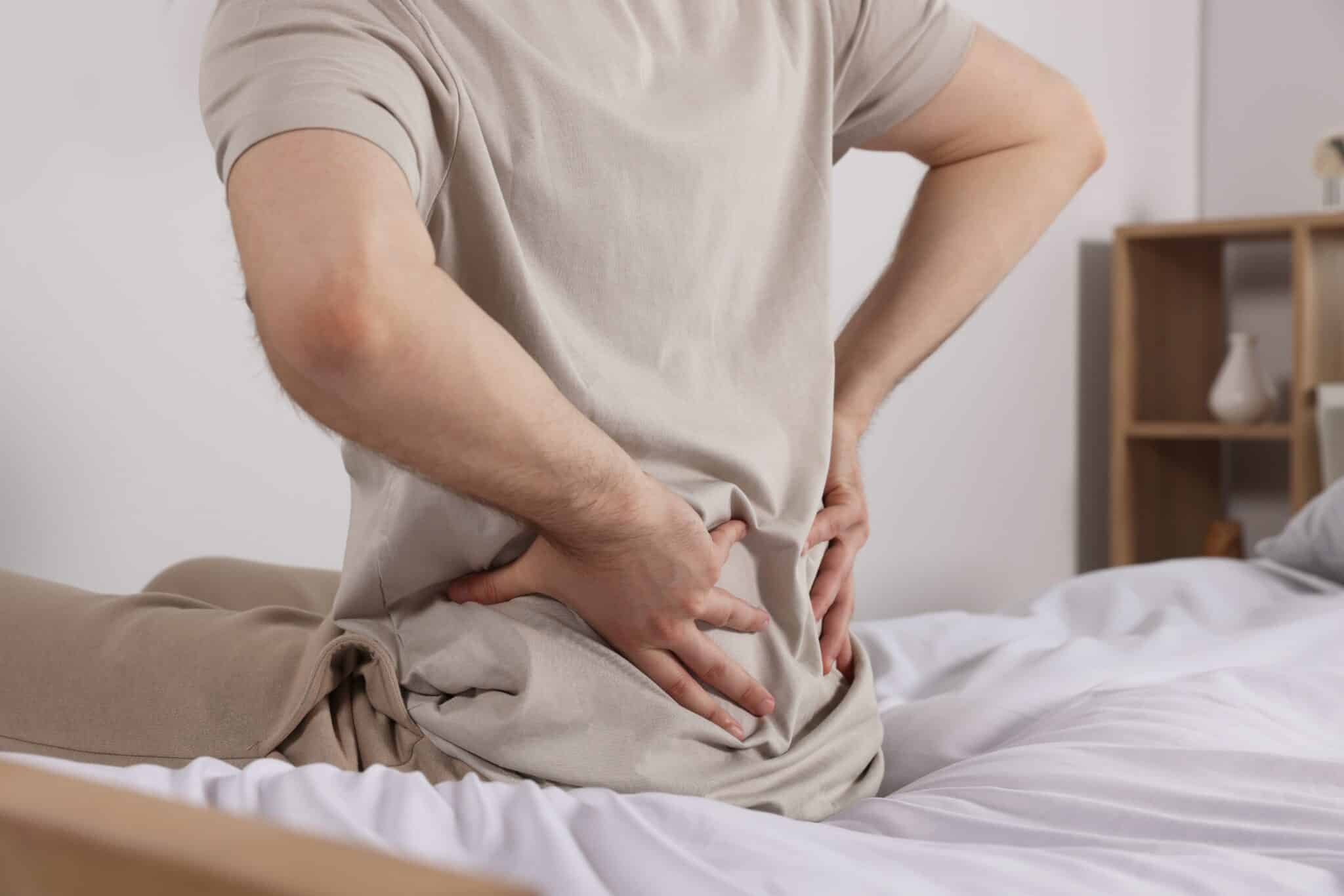 Man,Suffering,From,Back,Pain,While,Sitting,On,Bed,In
